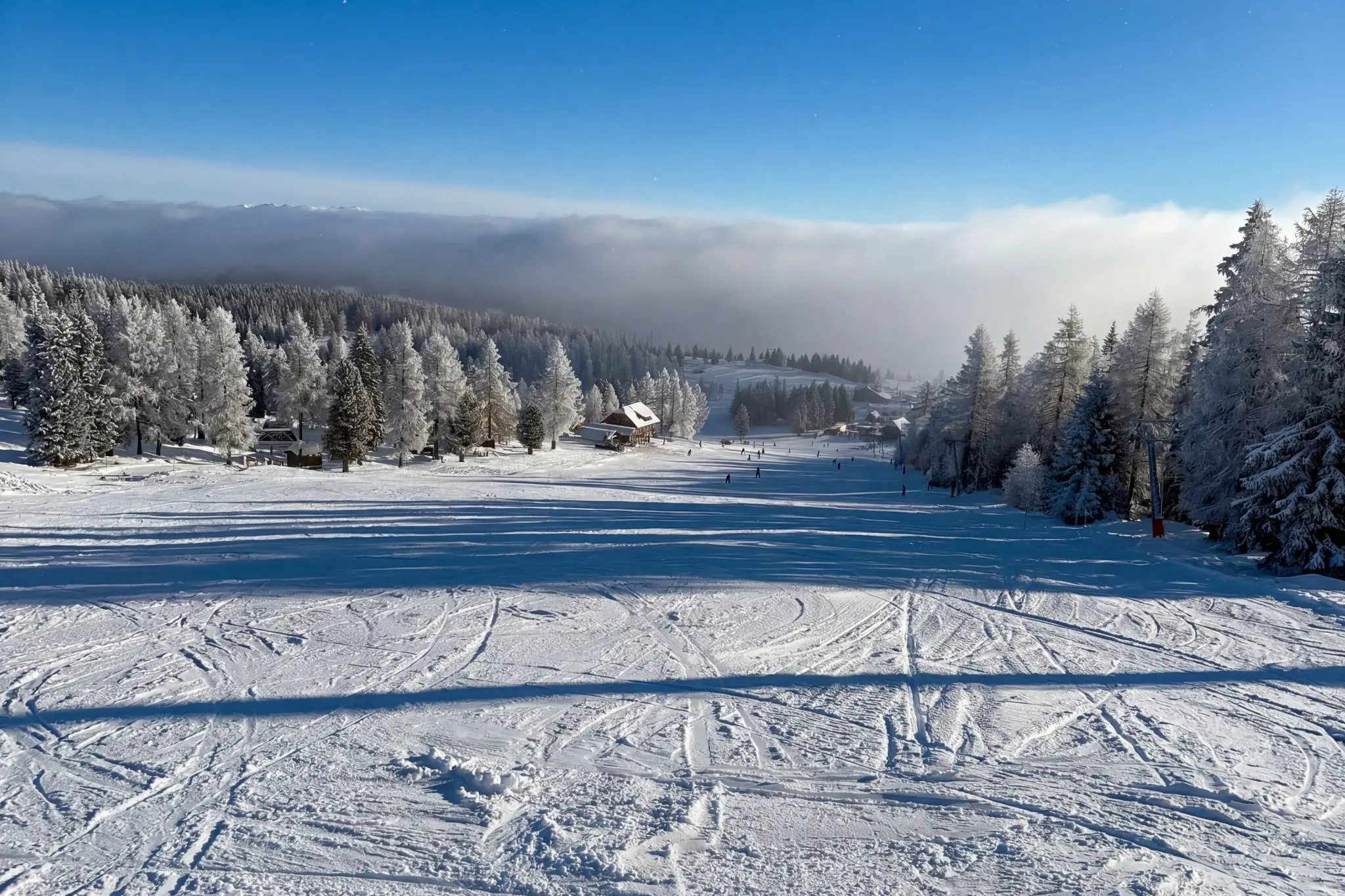 Skigebiet Hochrindl — Piste mit verschneitem Winterwald und blauem Himmel